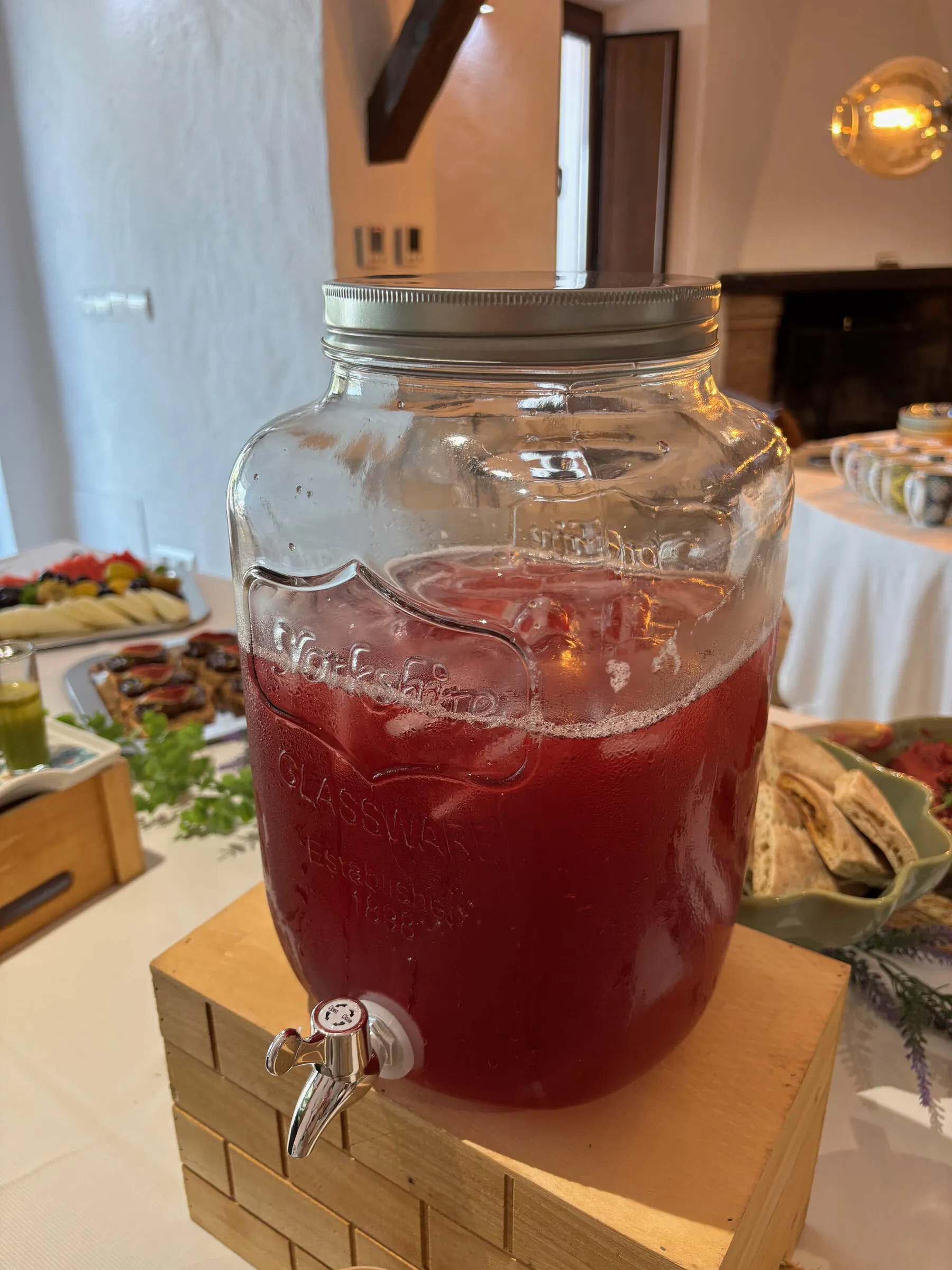A glass dispenser of deep red hibiscus infusion on a wooden crate